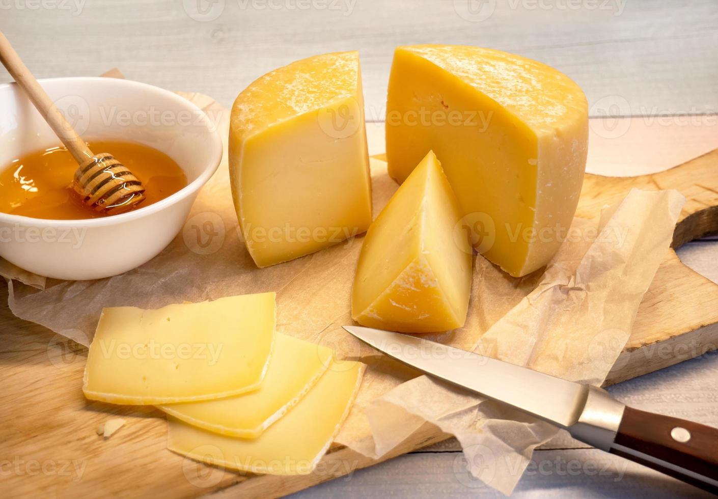 Handmade hard cheese. Natural farm cheese on an old wooden board with honey in a cup photo