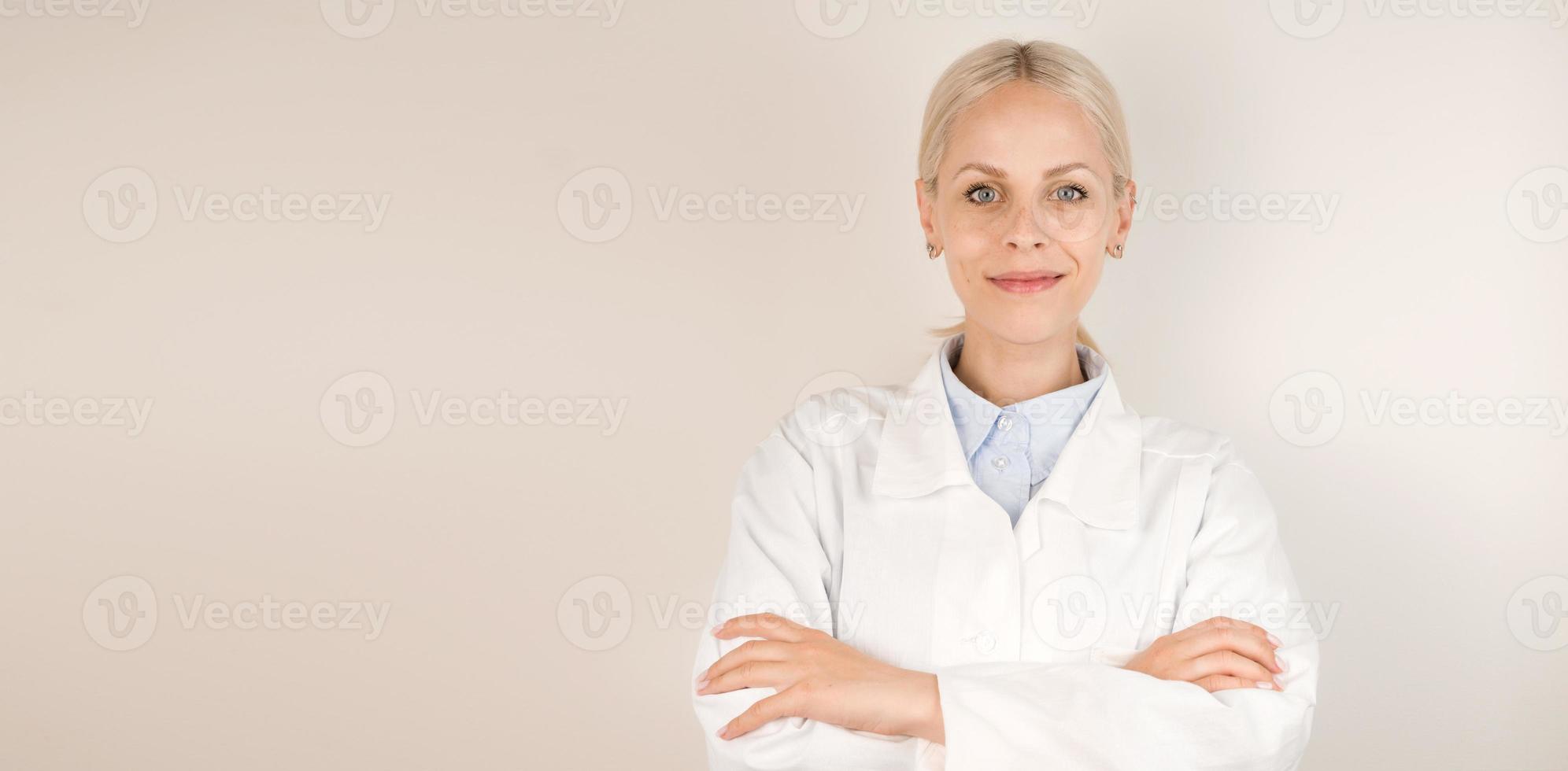 Young blonde doctor standing against gray background smiling at camera. Banner with place for text photo