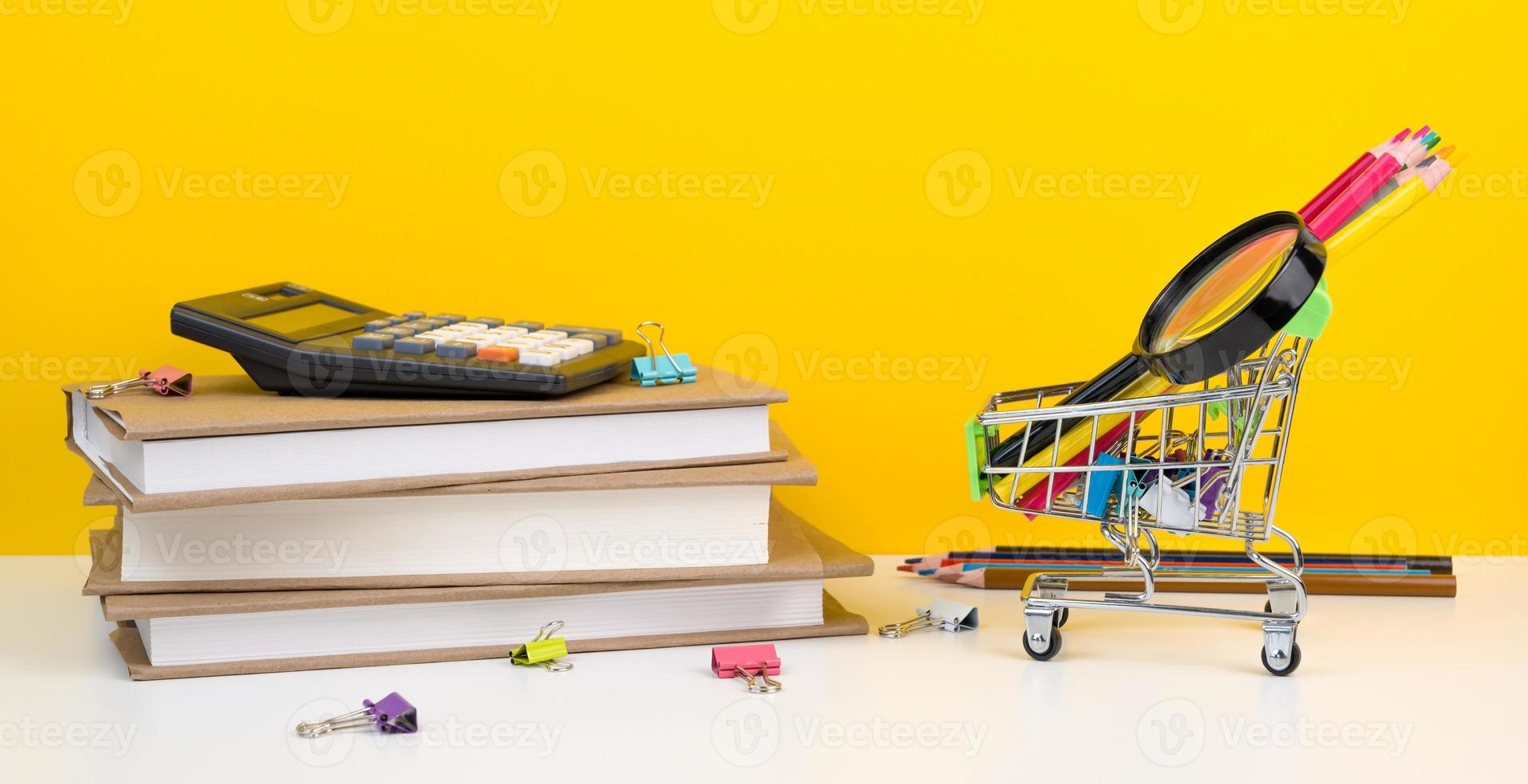 educación, regreso a la escuela. carrito de compras con suministros cerca de la pila de libros. foto