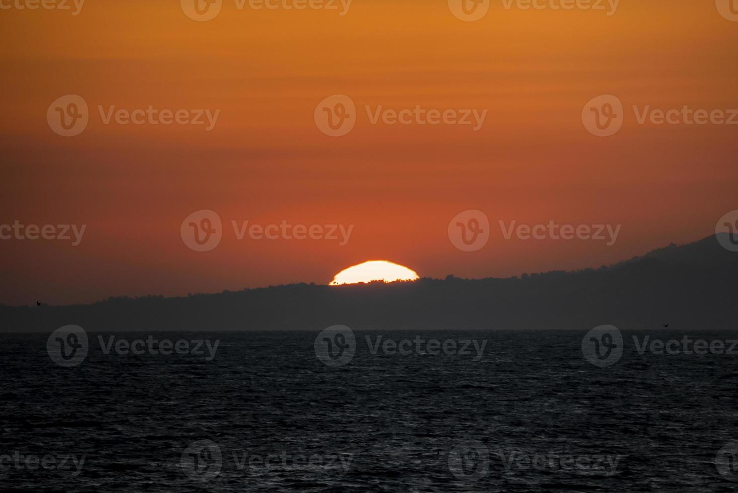 Tranquil view of beautiful seascape and sun setting behind silhouette mountain photo