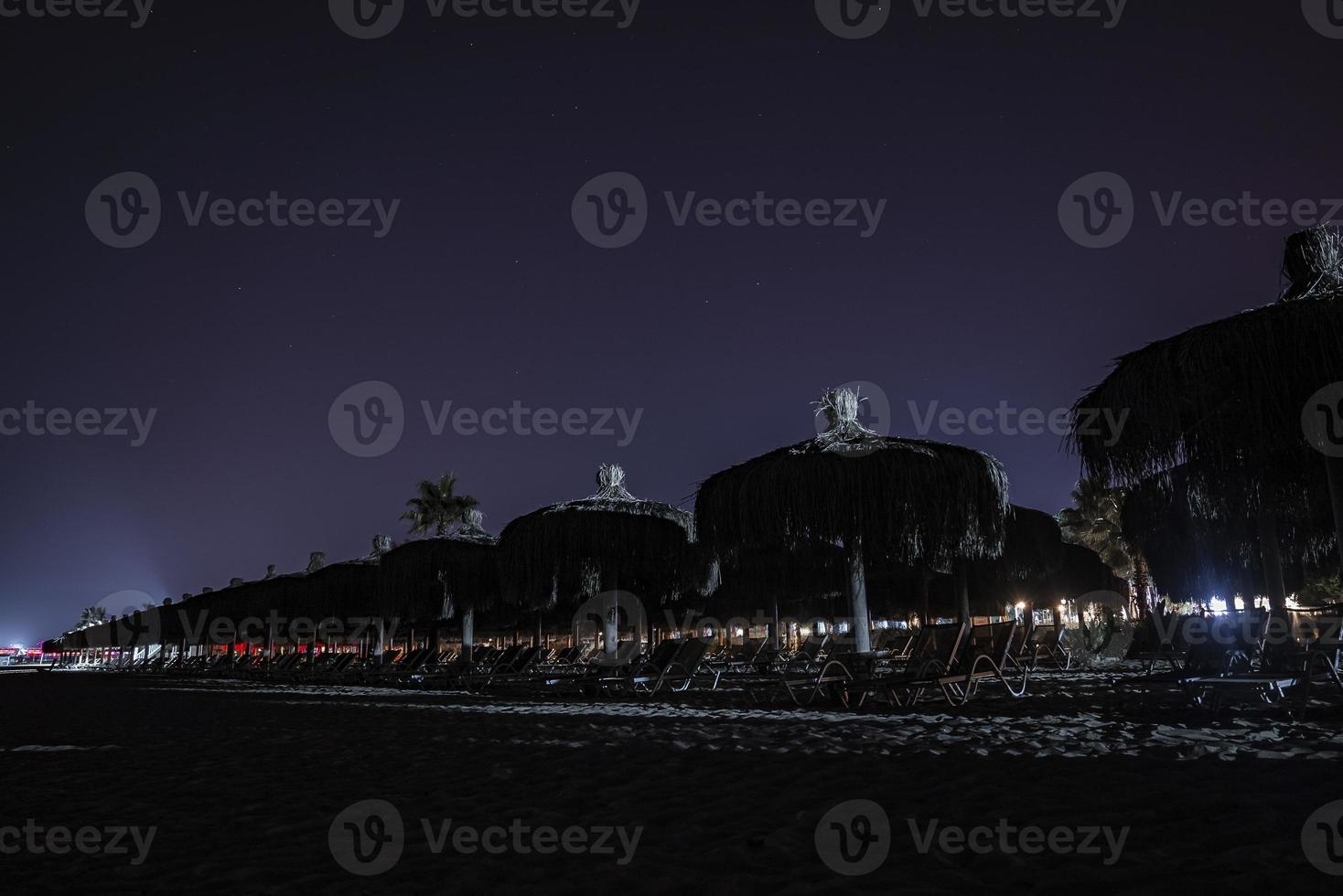 Empty deckchairs and thatched umbrellas arranged on beach at night photo
