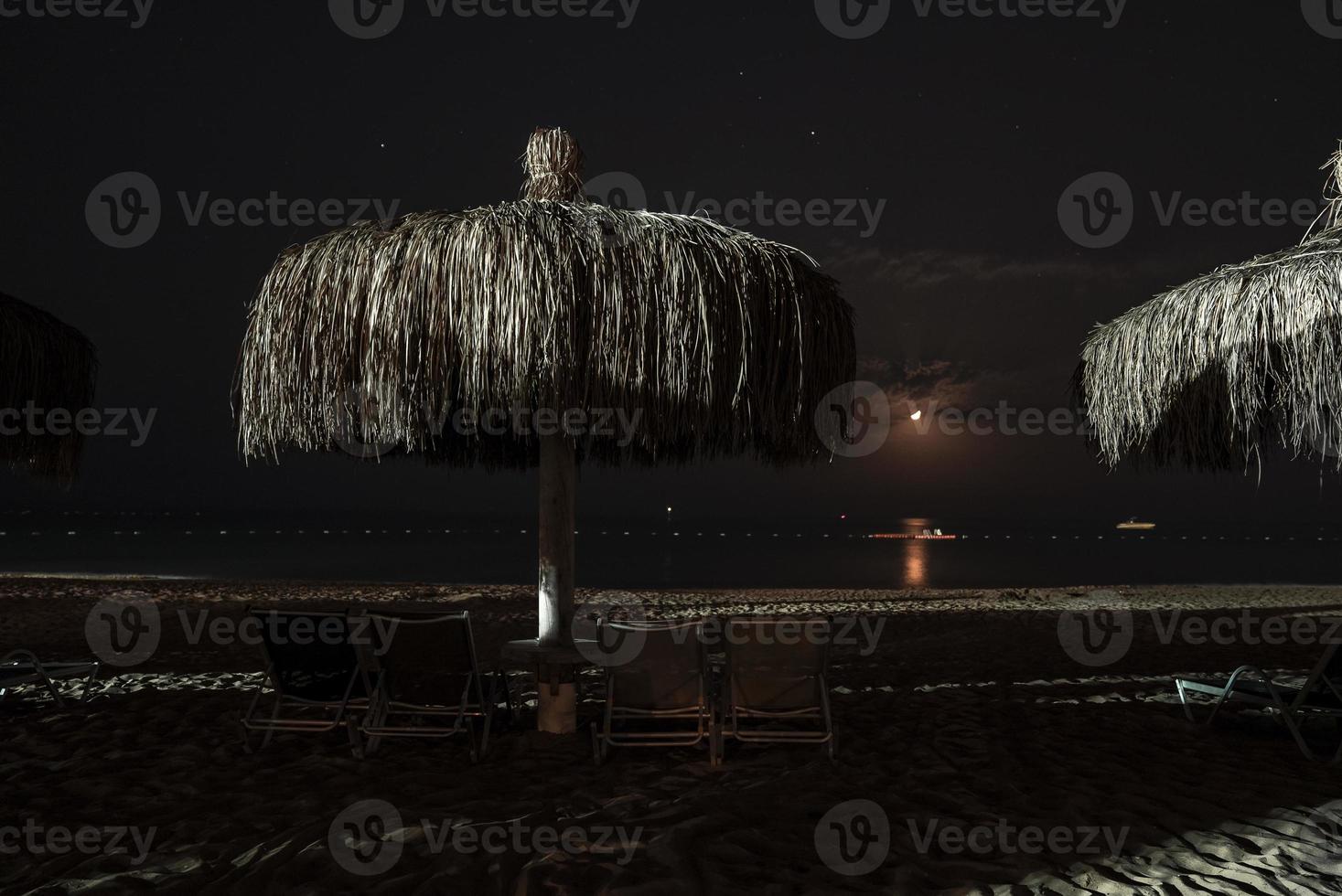 Loungers and thatched parasols arranged on sandy beach at night photo