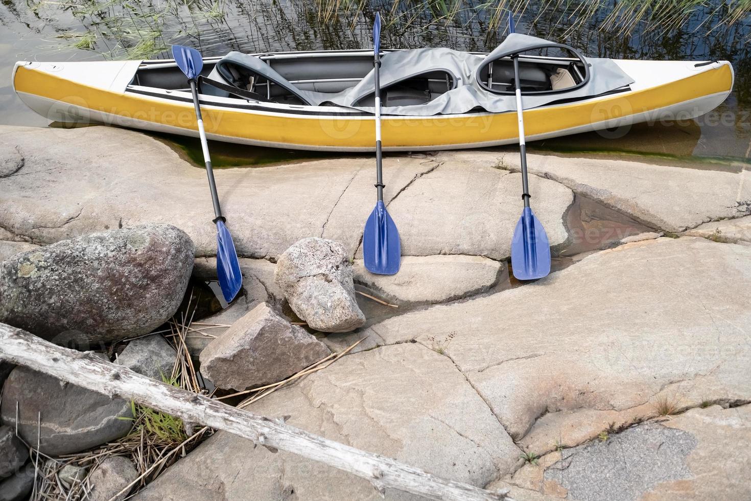 Three person kayak with paddles parked at the rocky shore of the lake, on a summer day. Active rest. photo