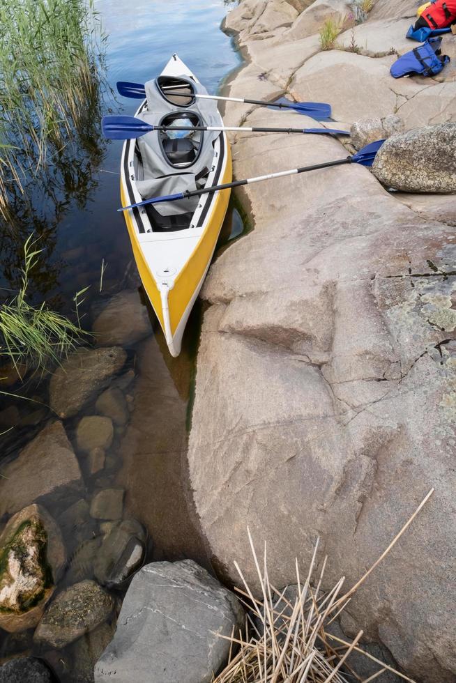 A three-seater kayak with oars is parked on the rocky shore of the lake with life jackets nearby, on a summer day. Active rest. photo