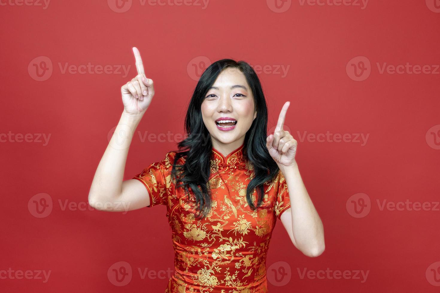 Asian woman with red cheongsam or qipao pointing to present for Chinese New Year celebration holiday isolated on red background concept photo