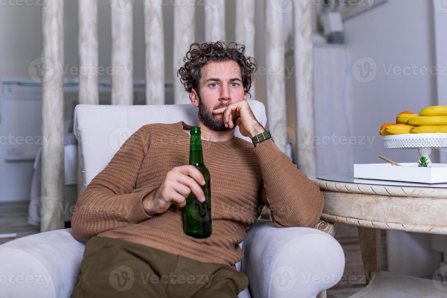 Sad sports fan sitting in an sofa and watching a match on television with his team losing the game . man watching football or soccer game on tv at home and drinking beer photo