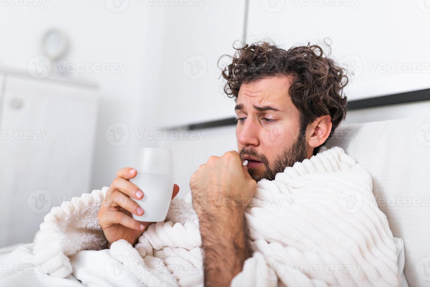 sick wasted man lying in bed wearing pajama suffering cold and winter flu virus having medicine tablets in health care concept Drinking pills with glass of water photo