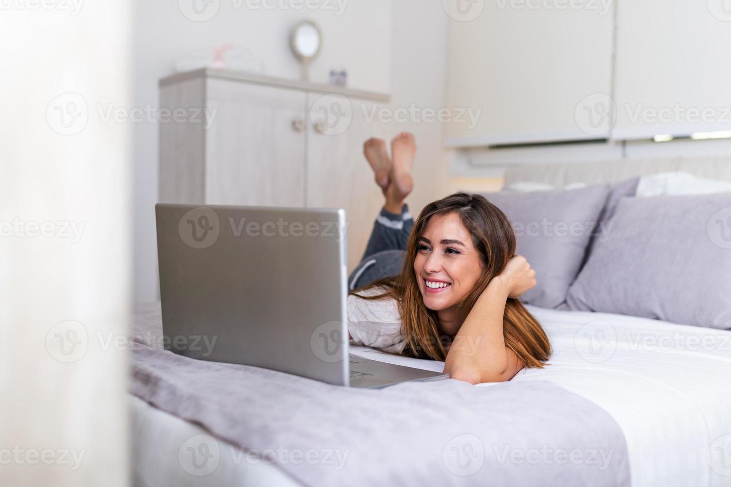 Beautiful Woman Relaxing On Bed Using Laptop Computer. Beautiful woman working on a laptop with smiling and lying down on the bed at a condominium in the morning. Freelancer girl working from home photo