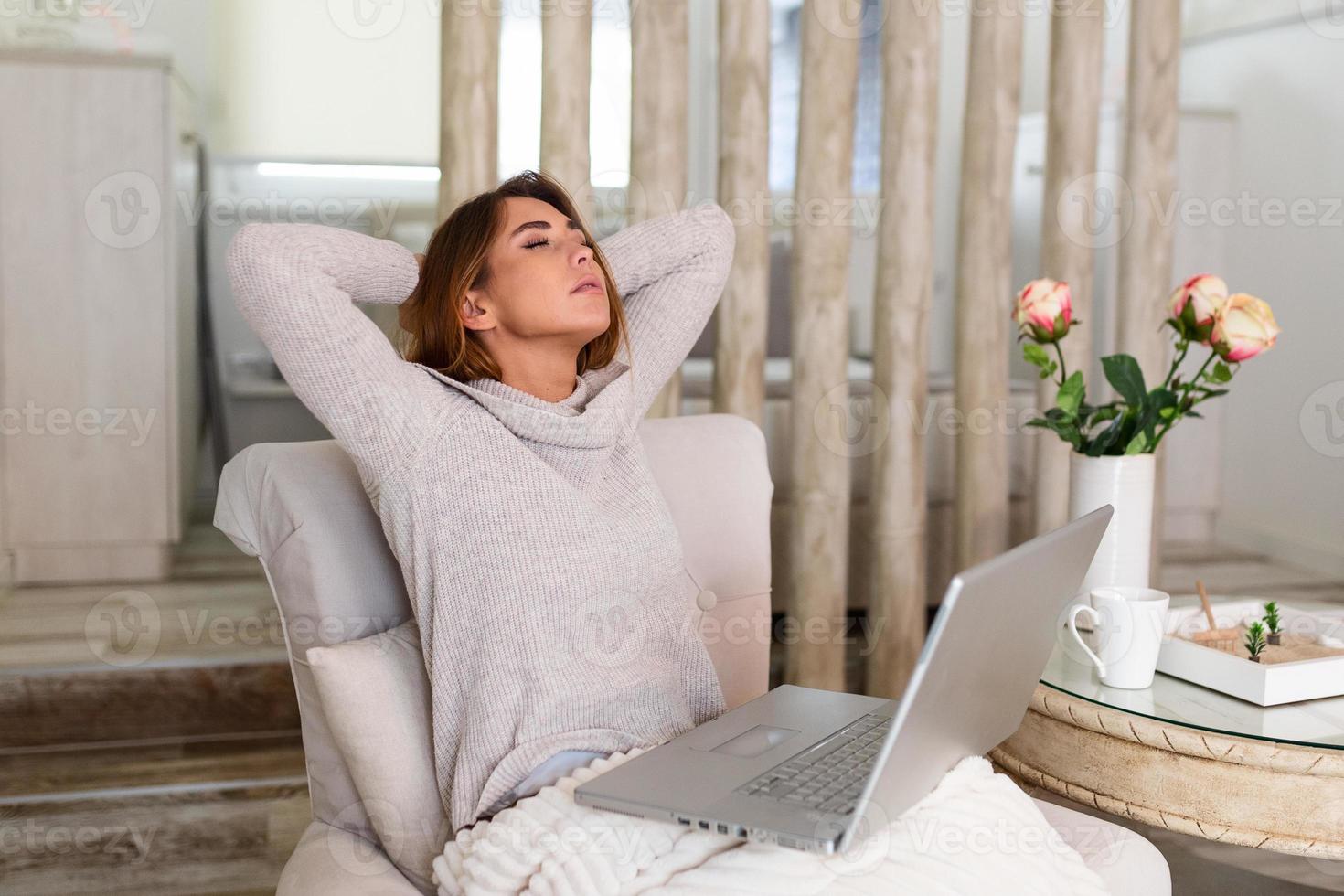 mujer joven con exceso de trabajo sentada en su casa con una computadora portátil frente a ella estirando los brazos por encima de la cabeza con los ojos cerrados para relajar los músculos, reducir la tensión, mejorar la visión, foto