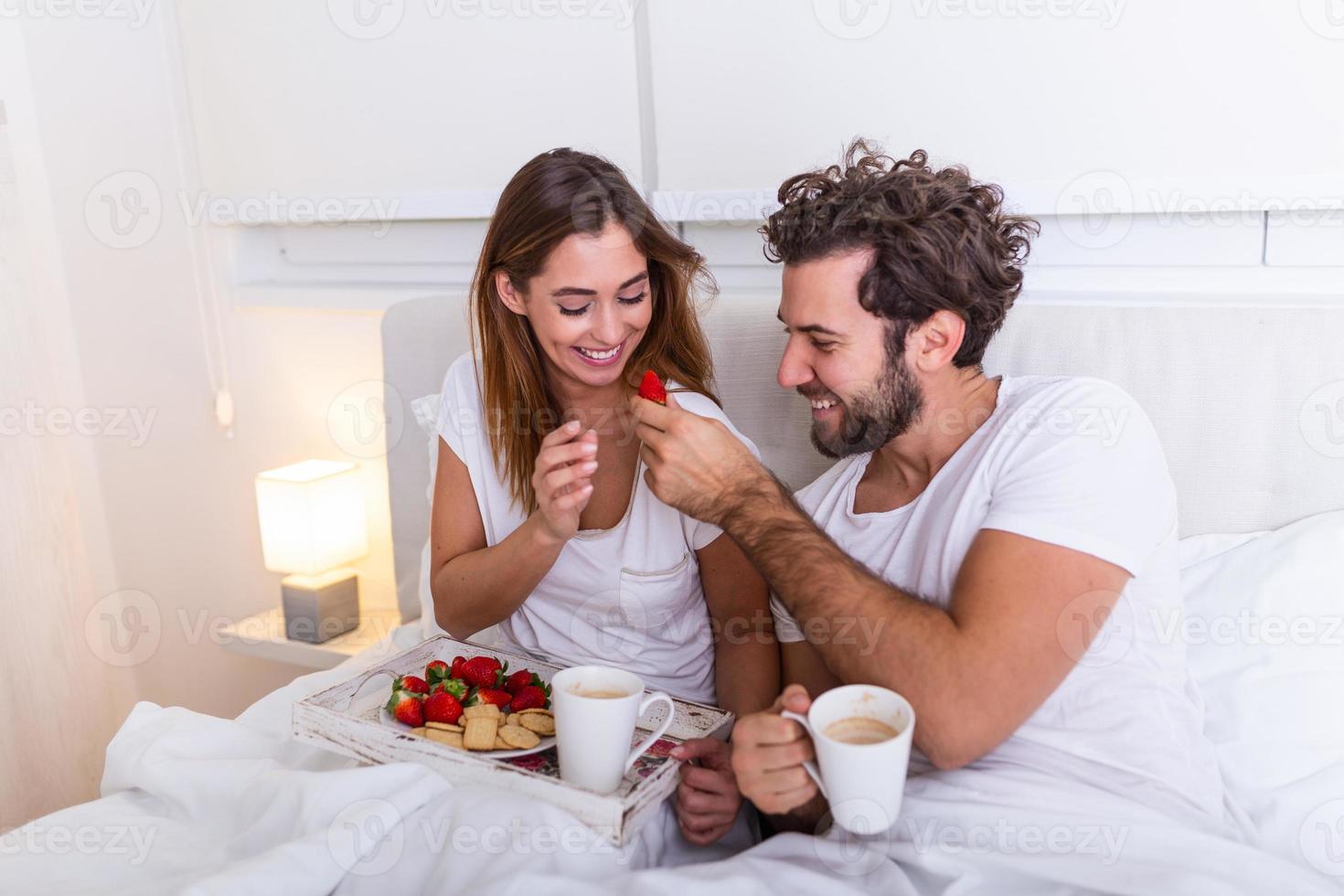 pareja enamorada desayunando en la cama. joven pareja caucásica desayunando romántico en la cama. hembra y macho, dos tazas de café, frutas y galletas coloridas. foto