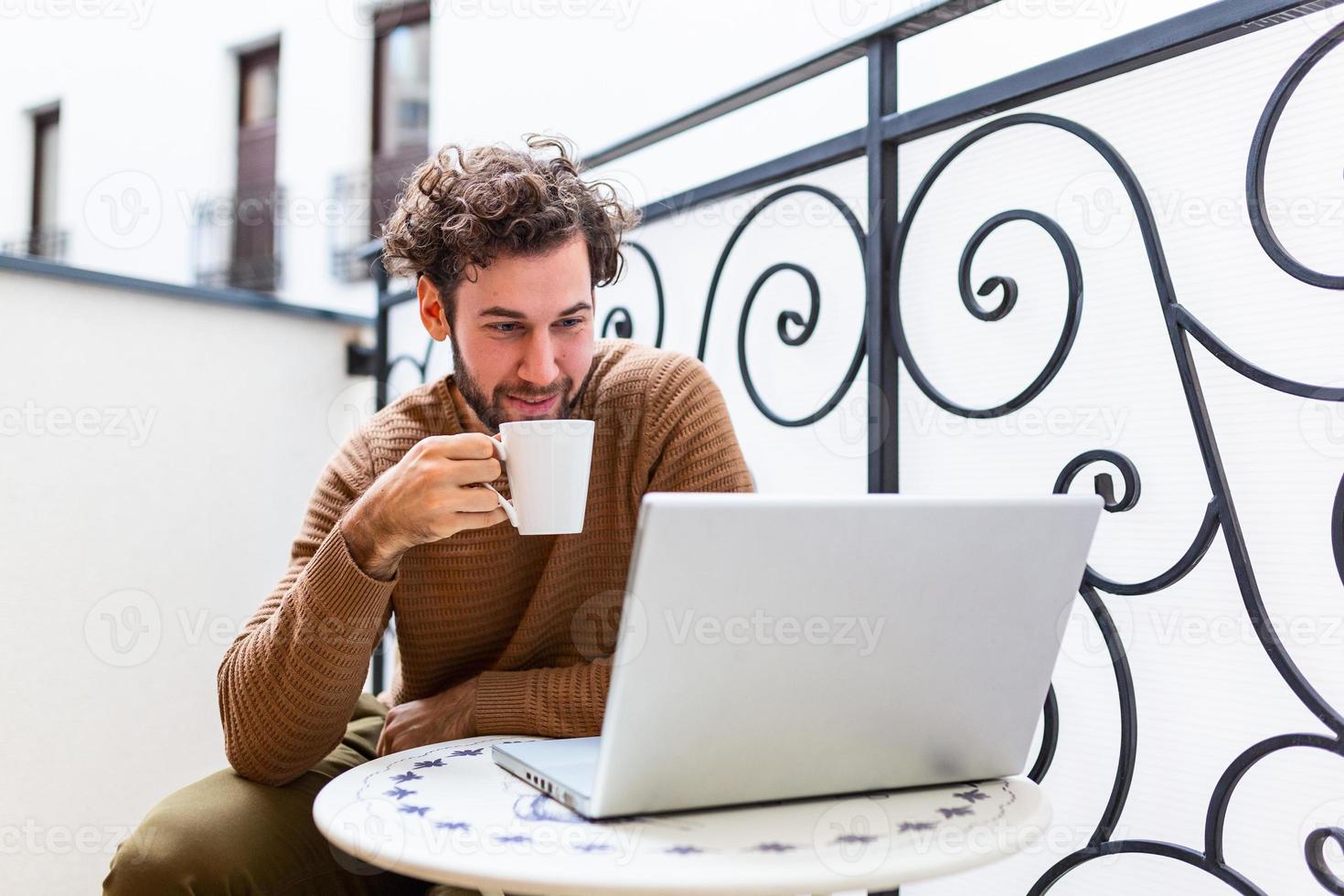 Young man checking his emails on laptop computer and drinking coffee in the morning. Working From Home concept photo