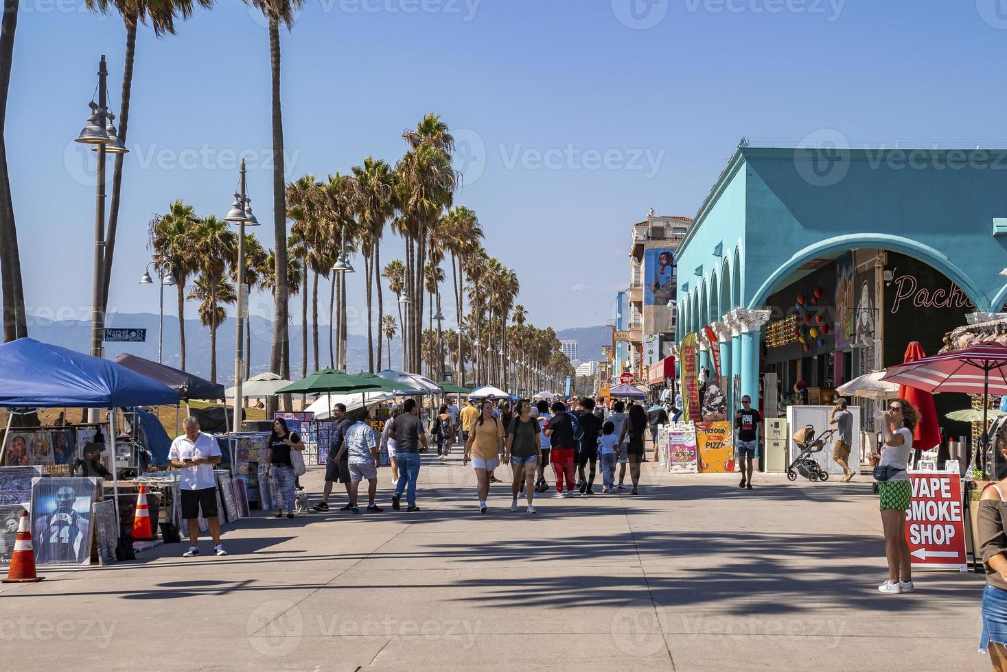 turistas caminando por el paseo marítimo de palmeras y edificios en la playa de Venecia foto