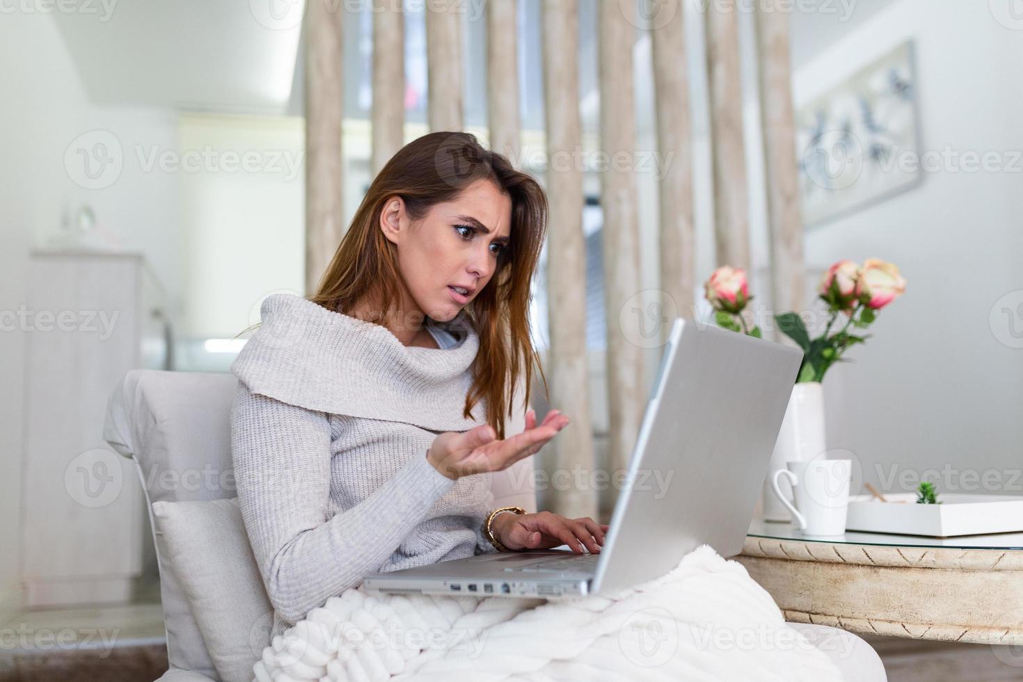 Attractive mad woman sitting at her sofa at home, looking at laptop screen with angry expression. Too much workload, file error, all data failed, forgot to save document photo