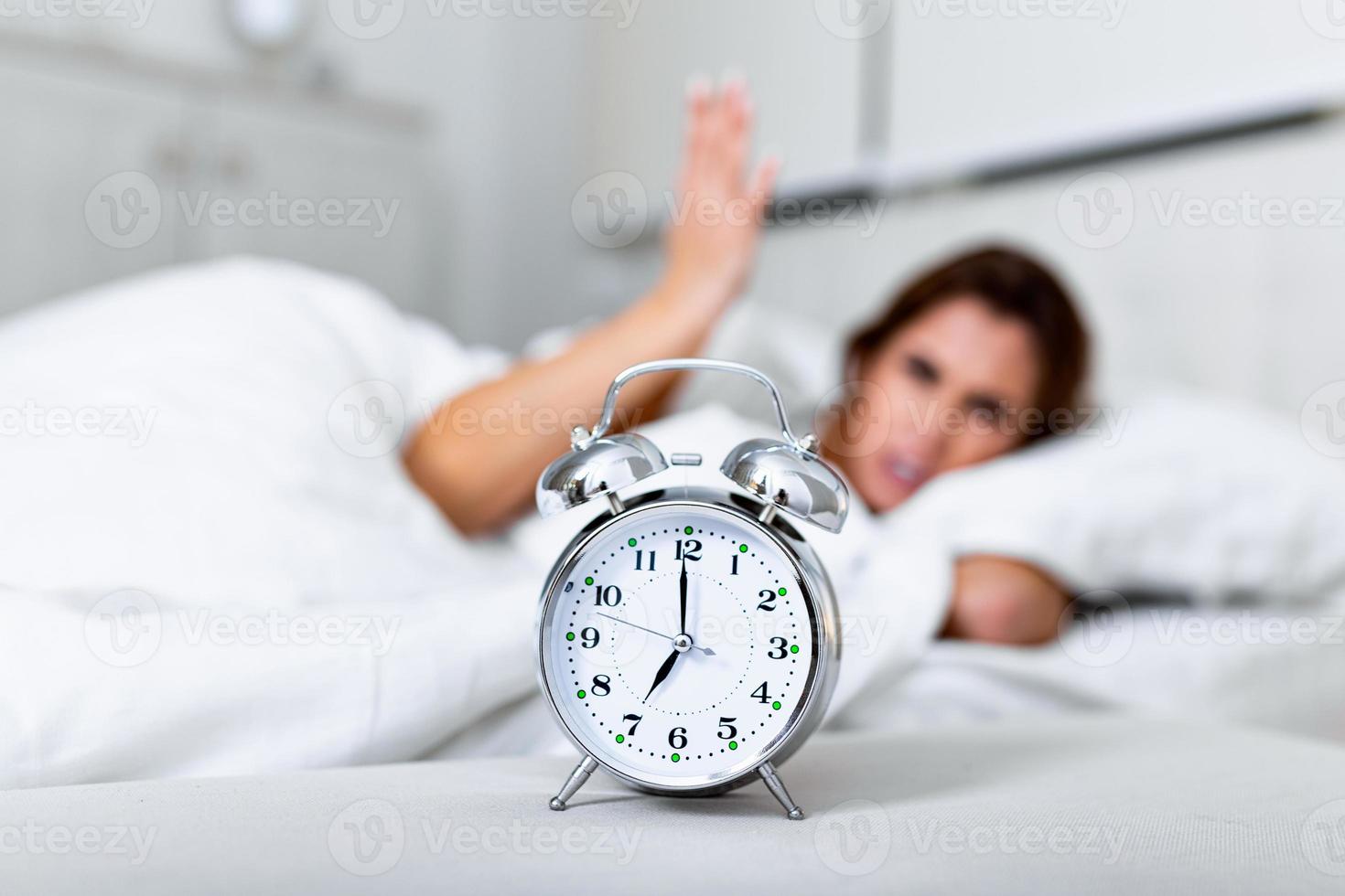 Wake up of an asleep girl stopping alarm clock on the bed in the morning. woman sleeping and wake up to turn off the alarm clock in the morning photo