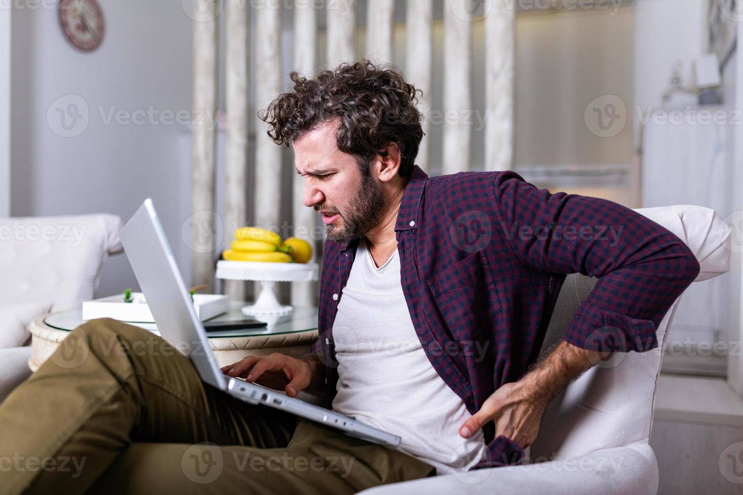 Tired millennial freelance worker stretch in sofa suffer from sitting long in incorrect posture, male employee have back pain or spinal spasm working in uncomfortable position. Sedentary life concept photo