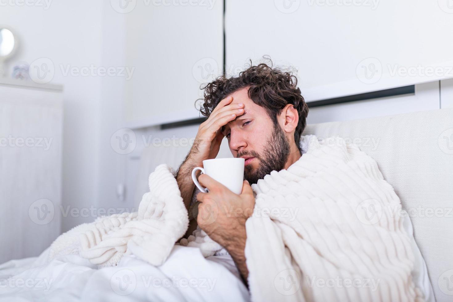 Man being sick having flu lying in bed checking his temperature and drinking hot beverage. Sick Man lying in bed with high fever. Cold flu and migraine. photo