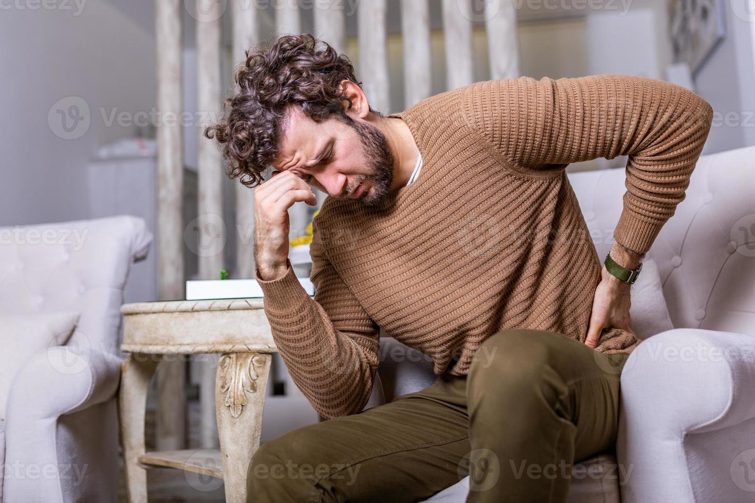 Tired man freelance worker stretch in sofa suffer from sitting long in incorrect posture, male employee have back pain or spinal spasm working in uncomfortable position. Sedentary life concept photo