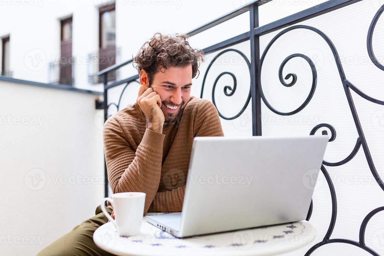 Happy young man smiling, as he works on his laptop to get all his business done early in the morning with his cup of coffee photo