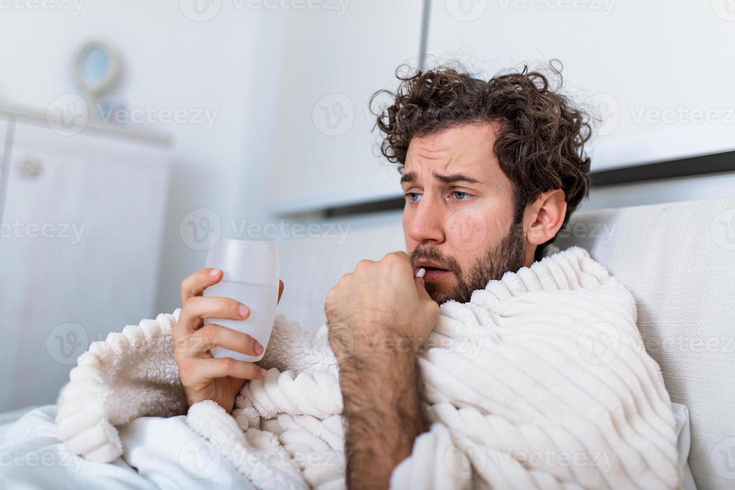 sick wasted man lying in bed wearing pajama suffering cold and winter flu virus having medicine tablets in health care concept Drinking pills with glass of water photo