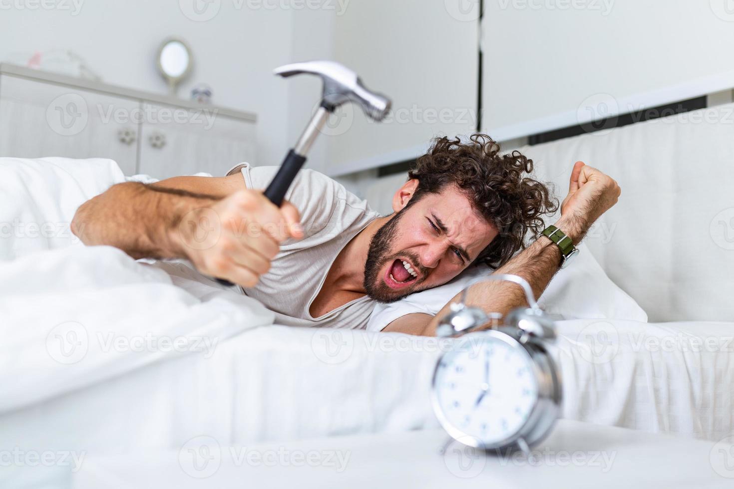 Young man tries to break the alarm clock with hammer, Destroy the Clock. Man lying in bed turning off an alarm clock with hammer in the morning at 7am. photo