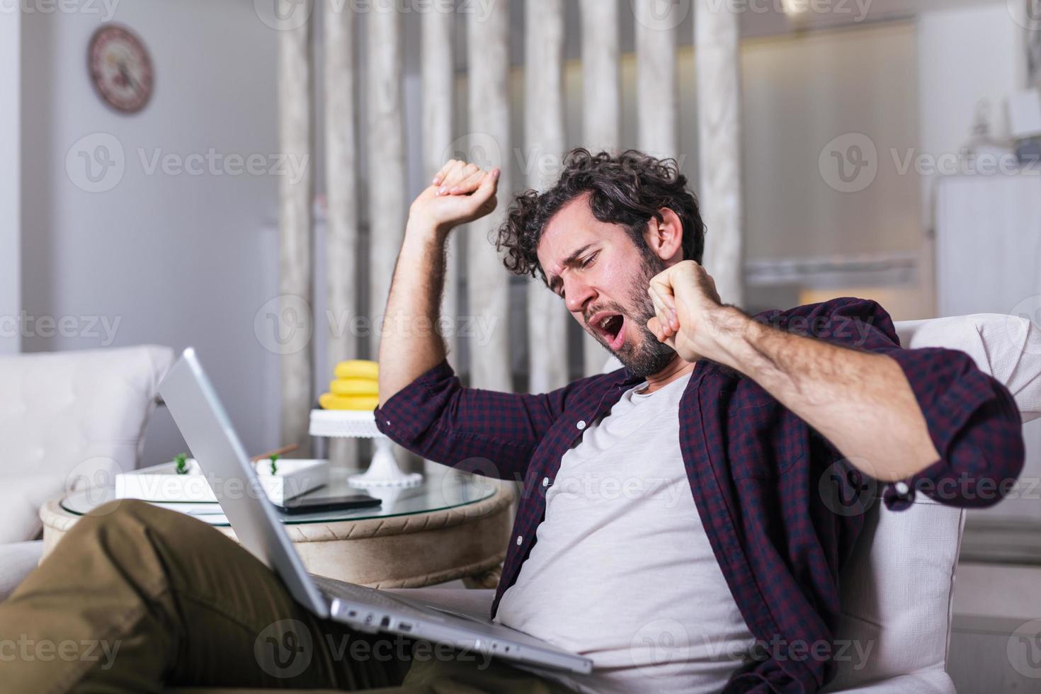 Early morning working. Sleepy tired freelancer is yawning at his home in front of the laptops screen on desk top photo