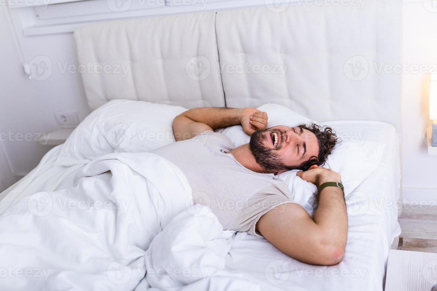 Young man sleeping waking up and stretching in his bed. people, bedtime and rest concept - man lying in bed at home, It's time to wake up photo