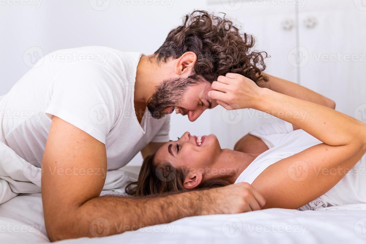 cariñosa joven pareja atractiva compartiendo un momento romántico en el dormitorio en casa. feliz pareja joven abrazándose y sonriendo mientras está acostado en la cama en un dormitorio en casa. foto