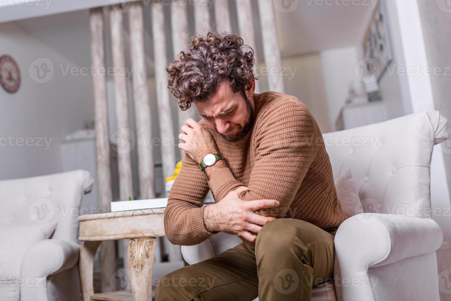 Man With Pain In Elbow. Pain relief concept. Handsome young man feeling the pain in hand elbow at home . Businessman's elbow pain, A young man touching her painful elbow photo