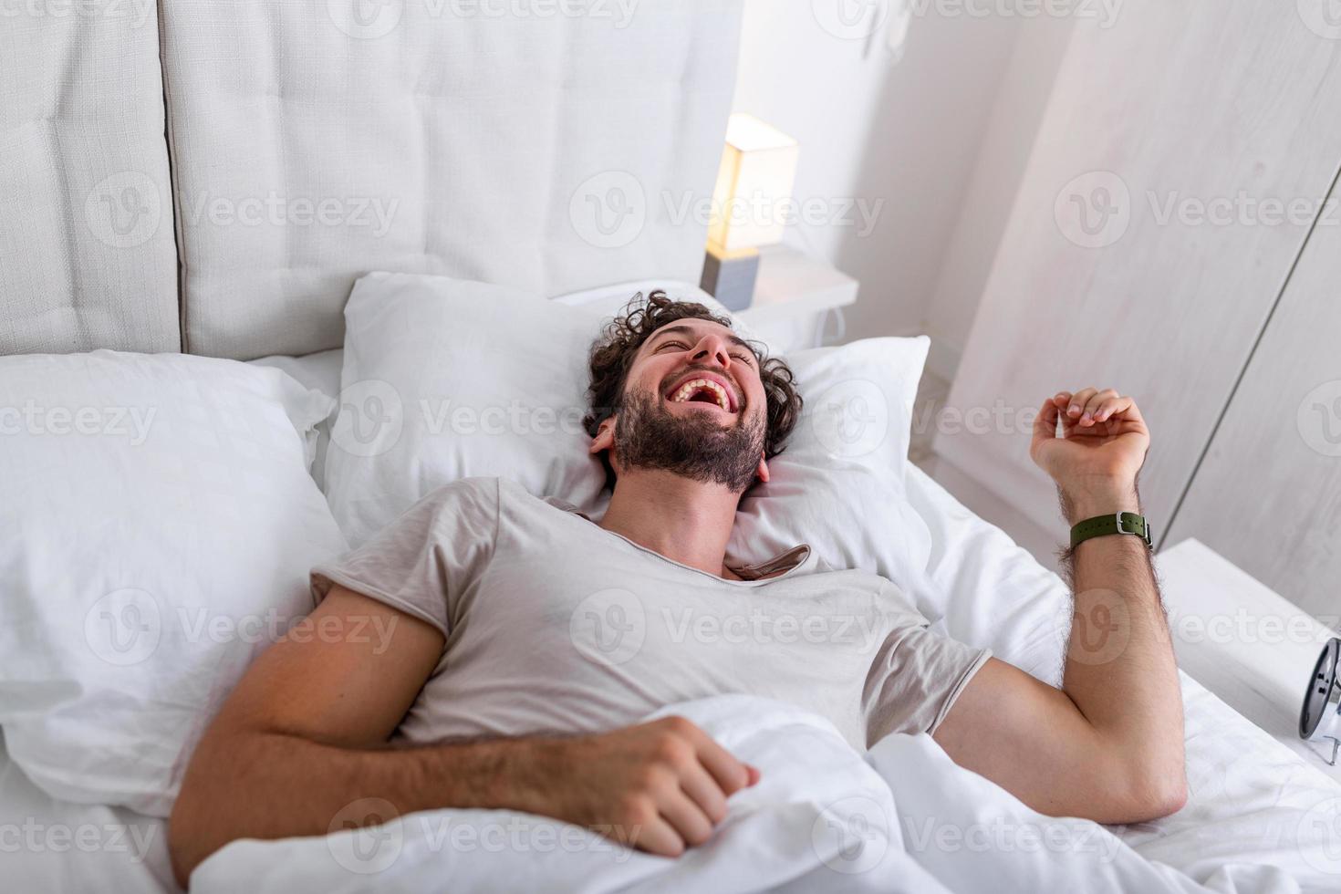 Young man sleeping waking up and stretching in his bed. people, bedtime and rest concept - man lying in bed at home, It's time to wake up photo