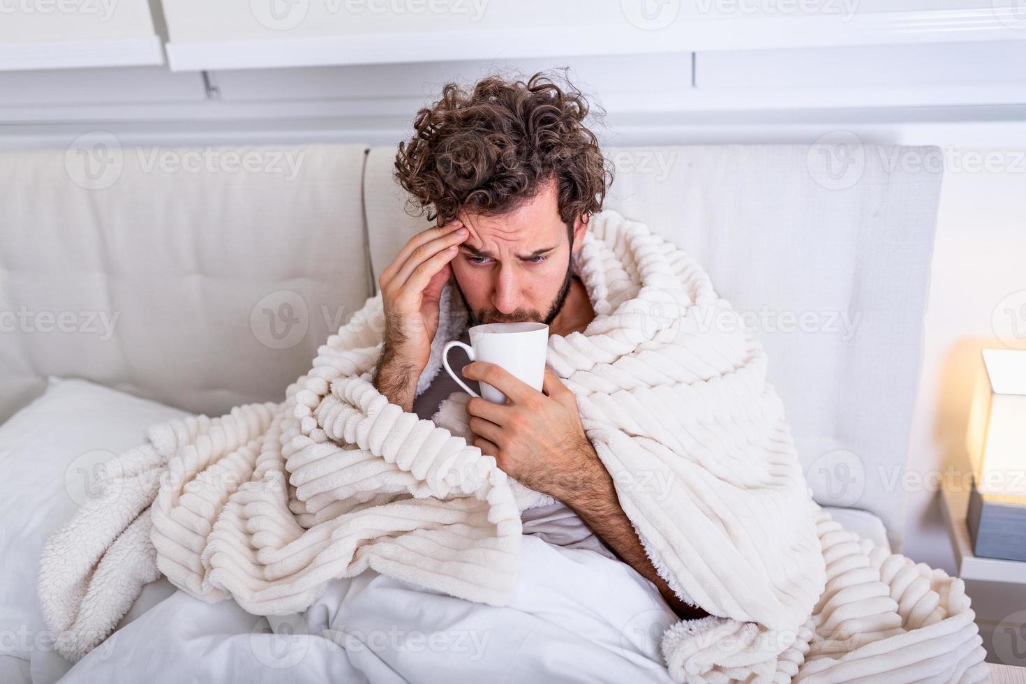 Portrait of a sick man with the flu, allergy, germs,cold coughing. Sick Man with headache sitting under the blanket with high fever and a flu, resting and drinking hot beverage photo