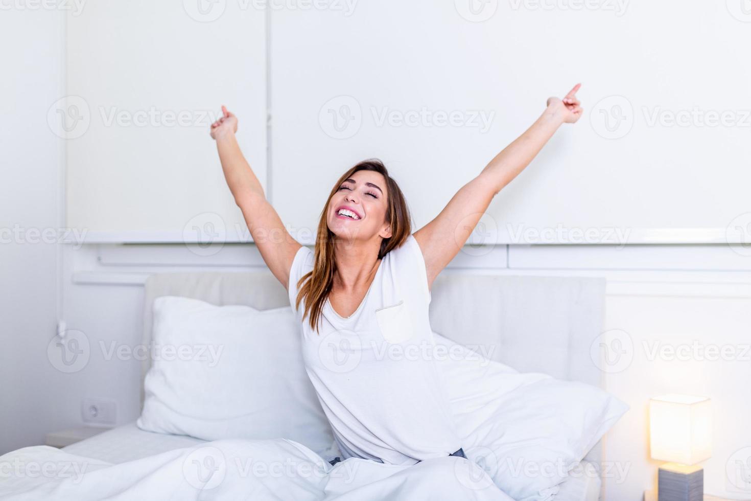 Woman stretching in bed after wake up, Pretty young woman in modern apartment stretching after wake up. Image of young smiling pretty lady lies in bed indoors. Eyes closed. photo