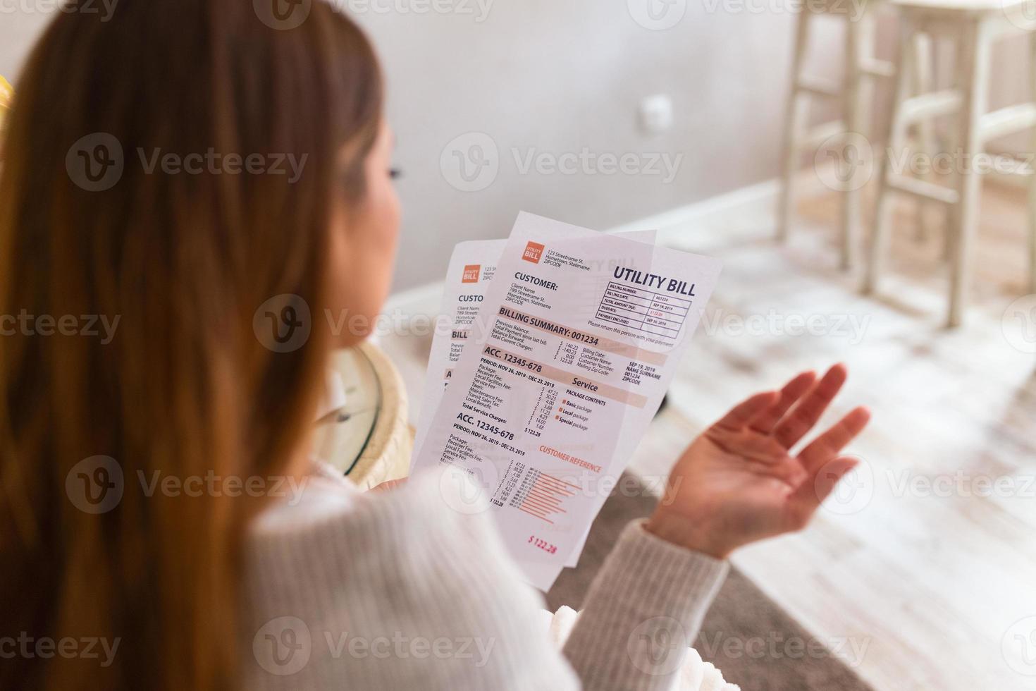 Indoor shot of casually dressed young woman holding papers in her hands, calculating family budget, trying to save some money , having stressed and concentrated look photo