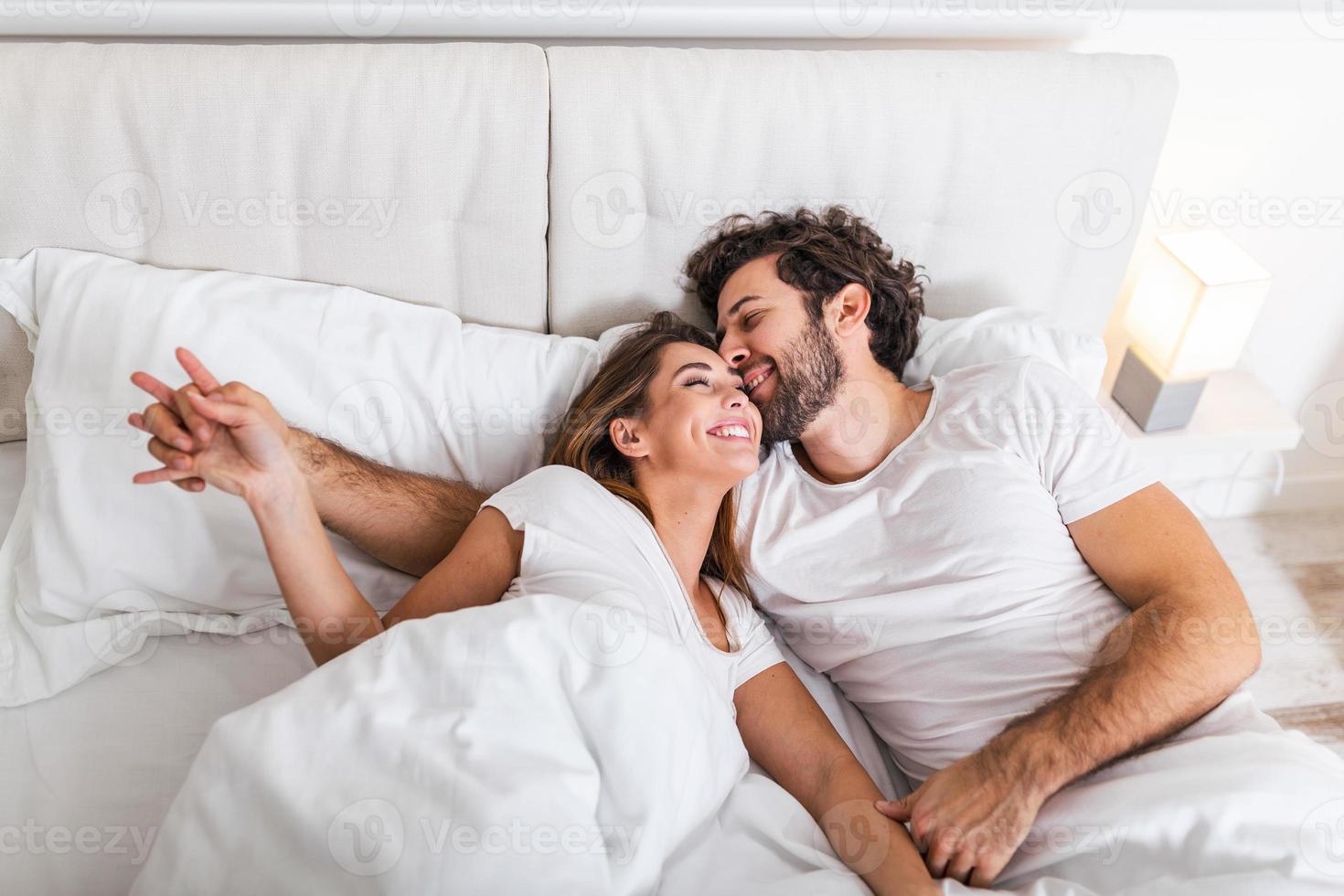 Happy couple is lying in bed together. Enjoying the company of each other.Happy young couple hugging and smiling while lying on the bed in a bedroom at home. photo