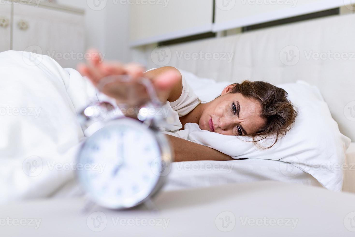 Woman lying in bed turning off an alarm clock in the morning at 7am. Hand turns off the alarm clock waking up at morning, girl turns off the alarm clock waking up in the morning from a call. photo