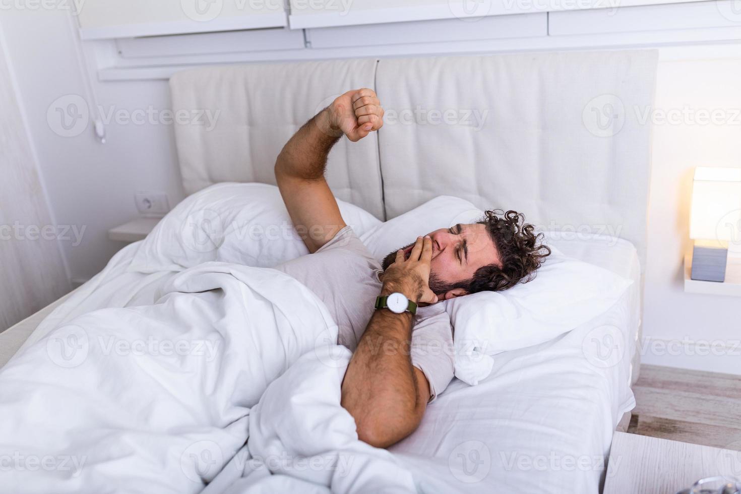 Young man stretching while waking up in the morning. Man yawning while waking up. Lazy young man in sleep. Portrait of man yawns and stretches in bed. photo