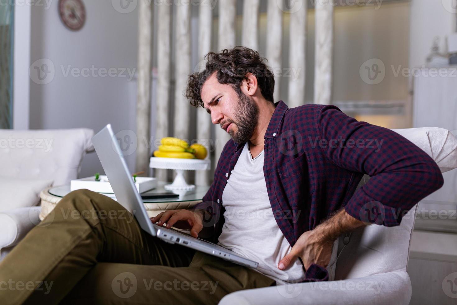 Tired man freelance worker stretch in sofa suffer from sitting long in incorrect posture, male employee have back pain or spinal spasm working in uncomfortable position. Sedentary life concept photo