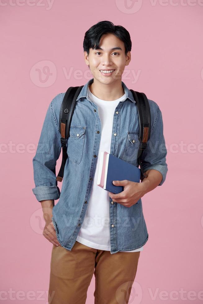 Smart guy student with backpack and bunch of books smiling at camera, copy space for advertisement over pink background photo