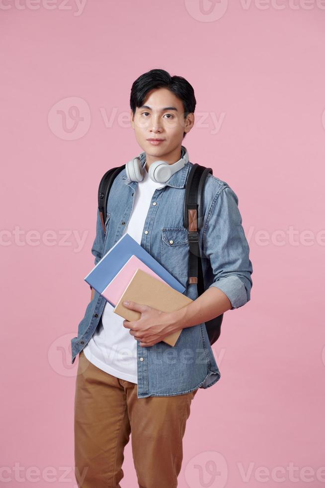 feliz estudiante sonriente de pie con mochila y carpetas sobre fondo rosa foto