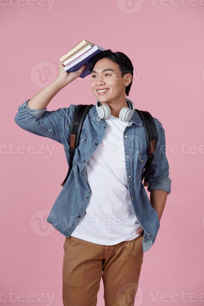 estudiante inteligente con mochila y un montón de libros sonriendo a la cámara, copiando espacio para publicidad sobre fondo rosa foto