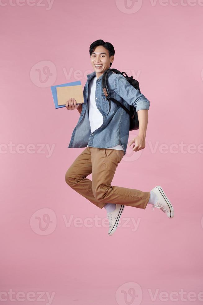 retrato completo de un divertido y alegre estudiante masculino saltando sobre fondo rosa foto