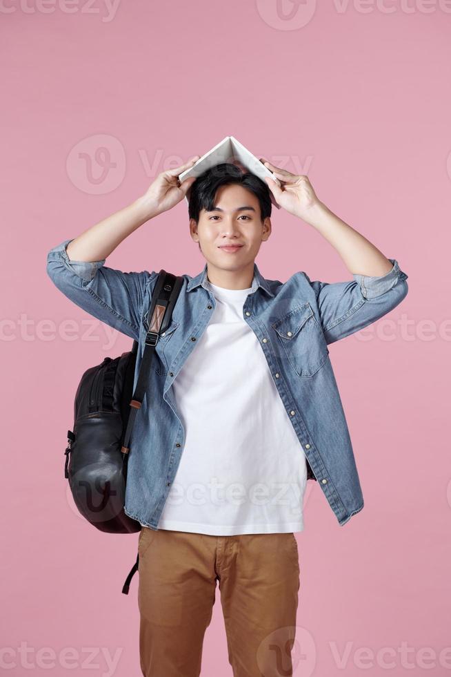 Young male student with open book on his head having fun isolated on a pink background photo