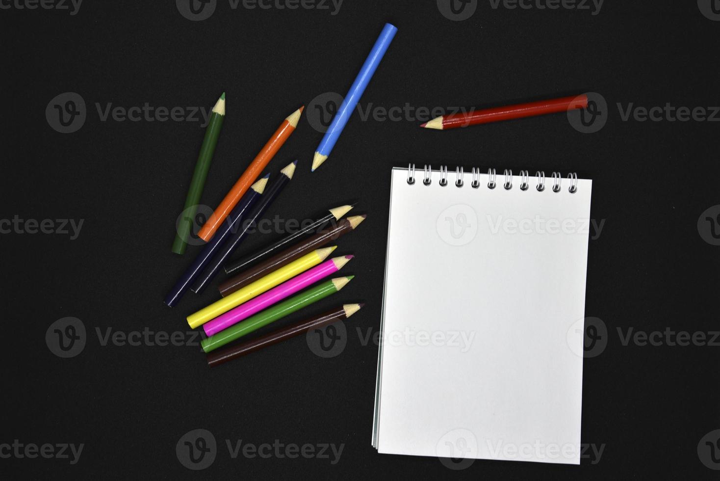 Colored pencils on a black background. Notepad and pencils. photo