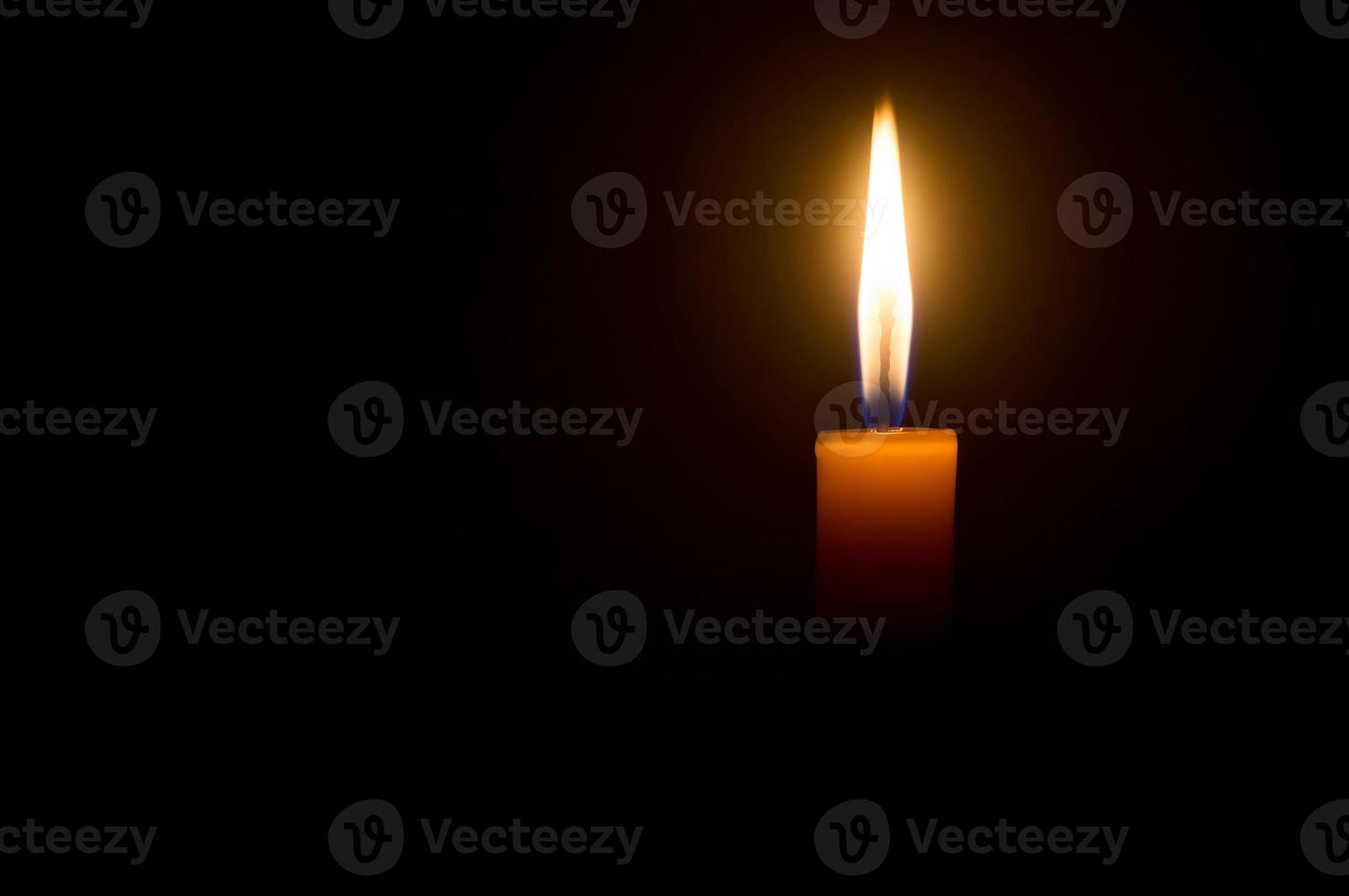 A single burning candle flame or light glowing on a yellow candl photo