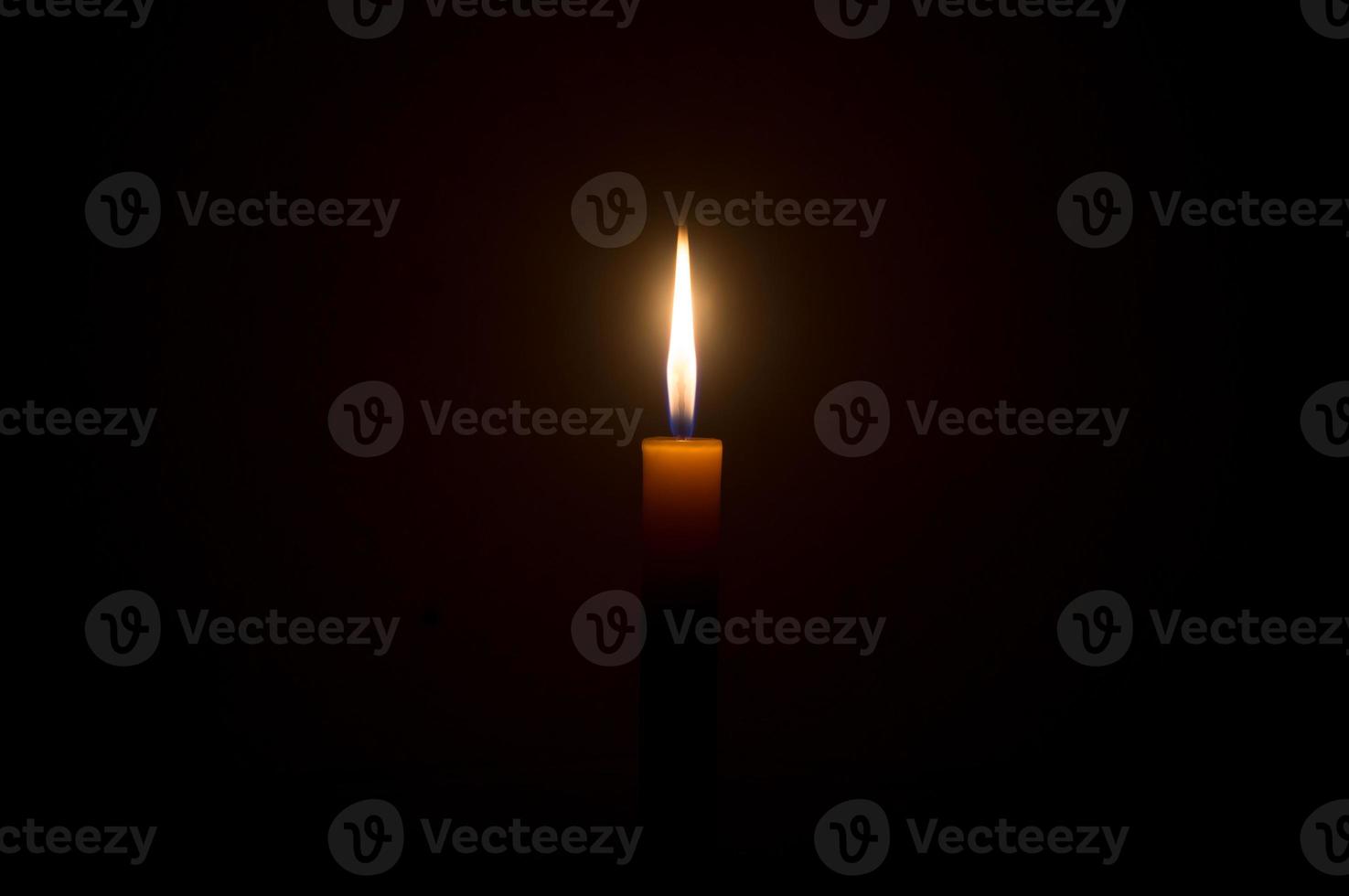A single burning candle flame or light glowing on a Single small yellow candle is isolated on black or dark background on table in church or temple for Christmas, funeral or memorial service photo