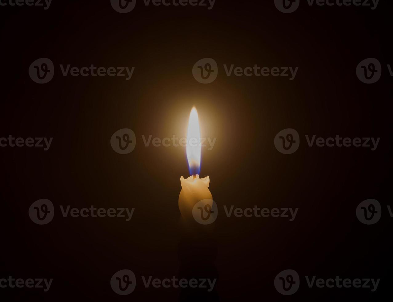 A single burning candle flame or light glowing on a spiral white candle on black or dark background on table in church for Christmas, funeral or memorial service photo