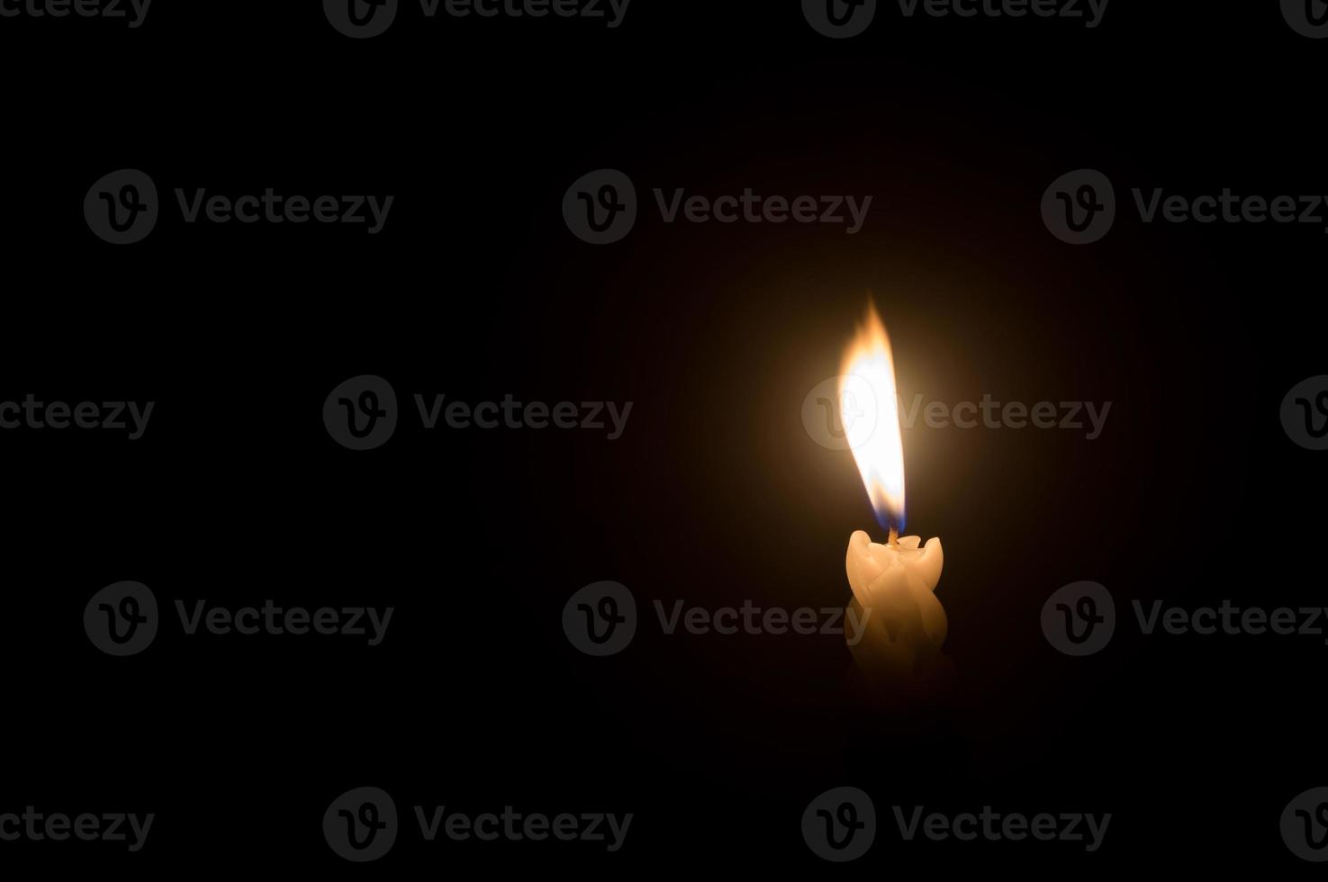 A single burning candle flame or light glowing on a spiral white candle against little blowing wind on black or dark background on table in church for Christmas, funeral or memorial service photo