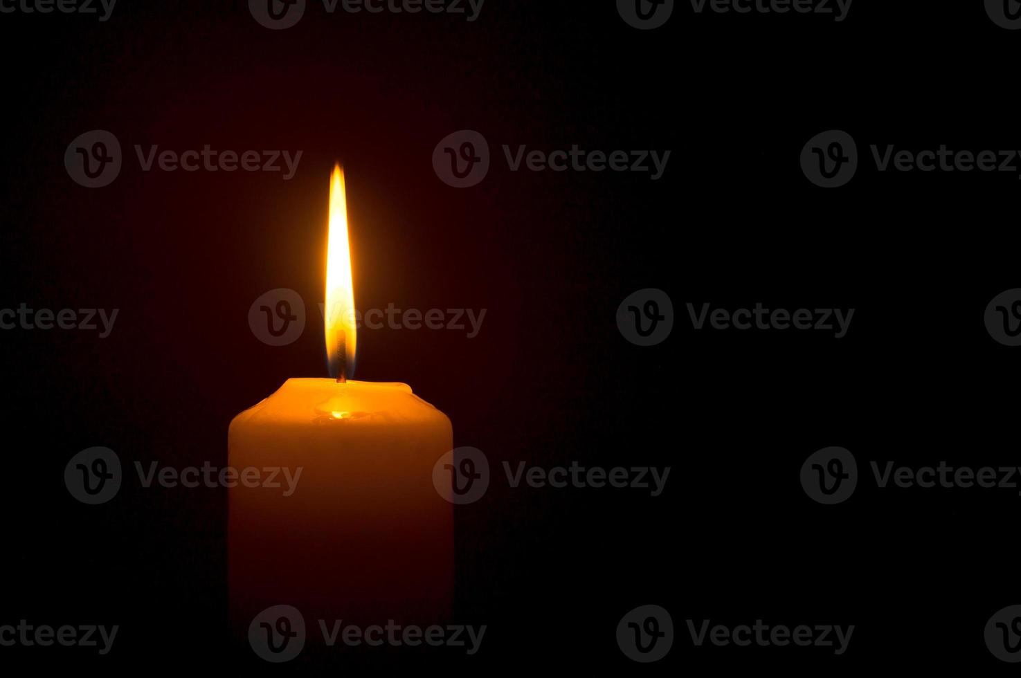 una sola llama o luz de vela encendida brilla en una vela amarilla sobre fondo negro u oscuro en la mesa de la iglesia para Navidad, funeral o servicio conmemorativo foto