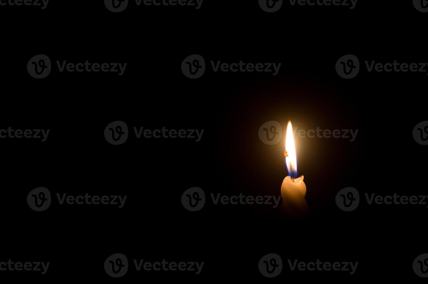 A single burning candle flame or light glowing on a spiral white candle on black or dark background on table in church for Christmas, funeral or memorial service photo