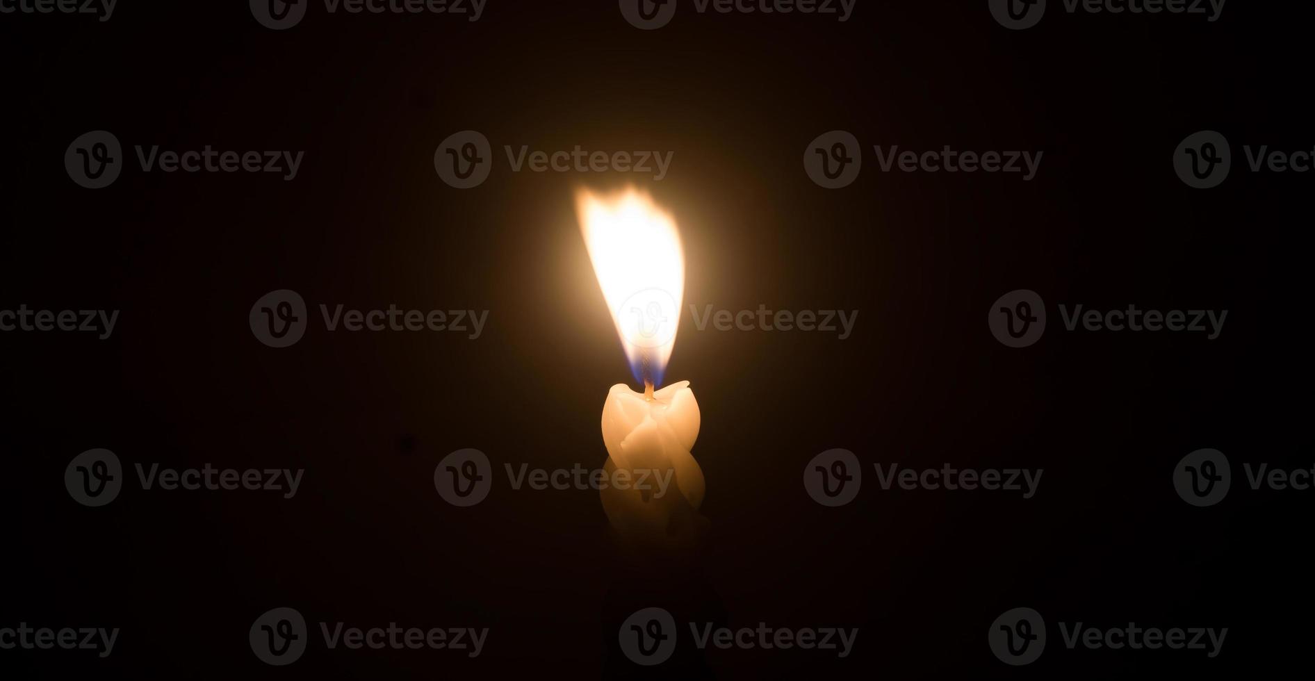 una sola llama de vela encendida o luz que brilla en una vela blanca en espiral contra un pequeño viento que sopla sobre fondo negro u oscuro en la mesa de la iglesia para Navidad, funeral o servicio conmemorativo foto