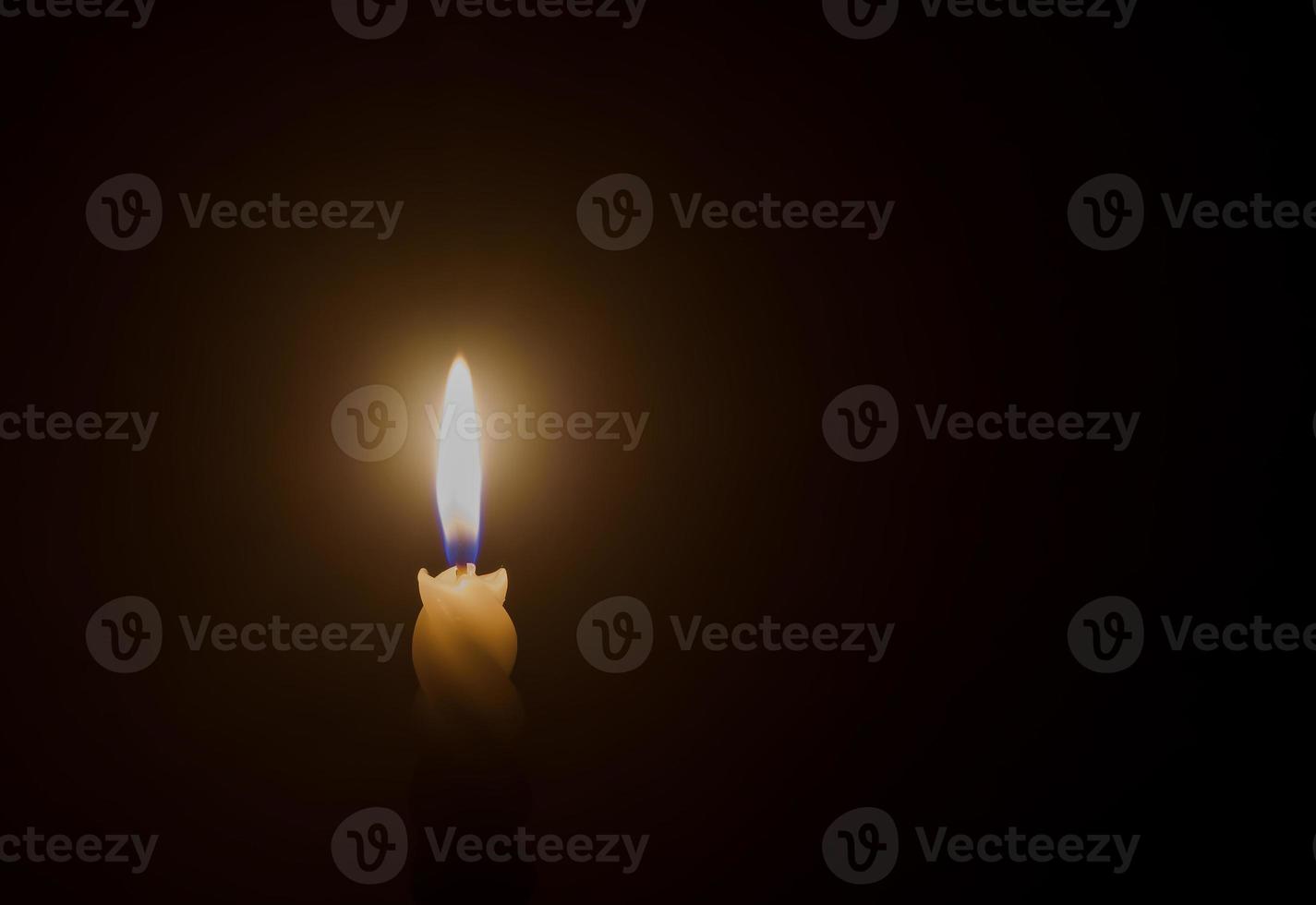 A single burning candle flame or light glowing on a spiral white candle on black or dark background on table in church for Christmas, funeral or memorial service photo